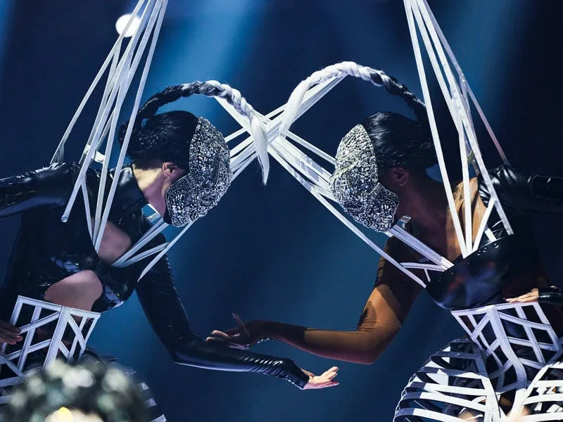 Awakening performers in geometric costumes connected by aerial ribbon rigging