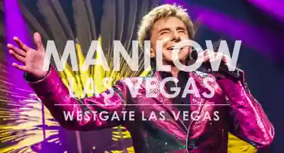 Barry Manilow seated at a piano under dark stage lighting in a purple jacket