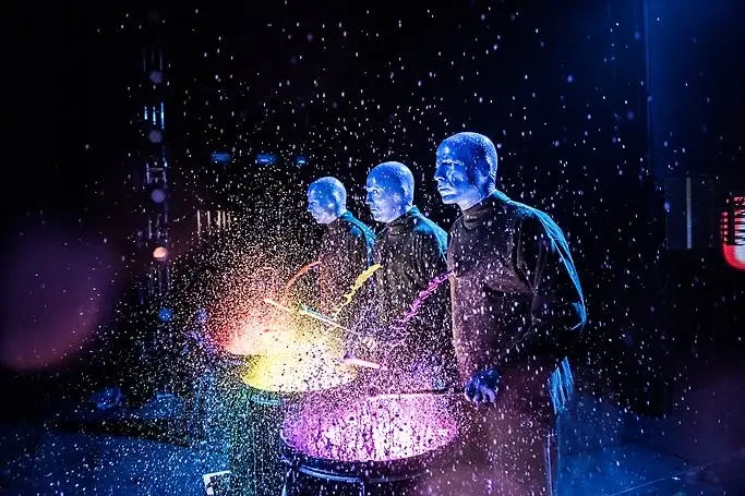 Blue Man Group three performers striking illuminated drums with water and sparks flying during Las Vegas show