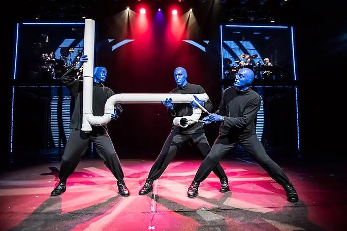 Blue Man Group performers on stage with oversized PVC pipes under red and blue stage lighting at Luxor Las Vegas