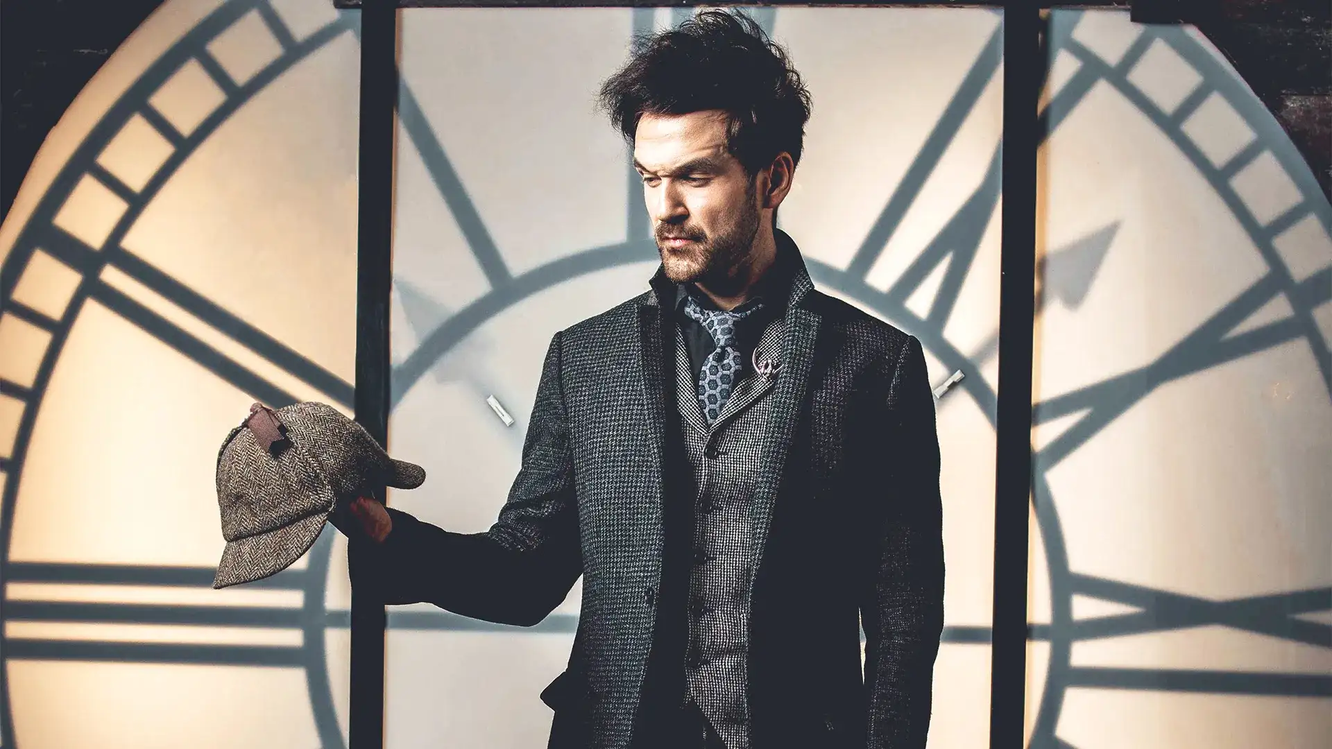 Colin Cloud in a dark houndstooth jacket holding a Sherlock Holmes-style deerstalker hat in front of a large illuminated clock face — promotional photo for Colin Cloud Mastermind at Harrah's Las Vegas