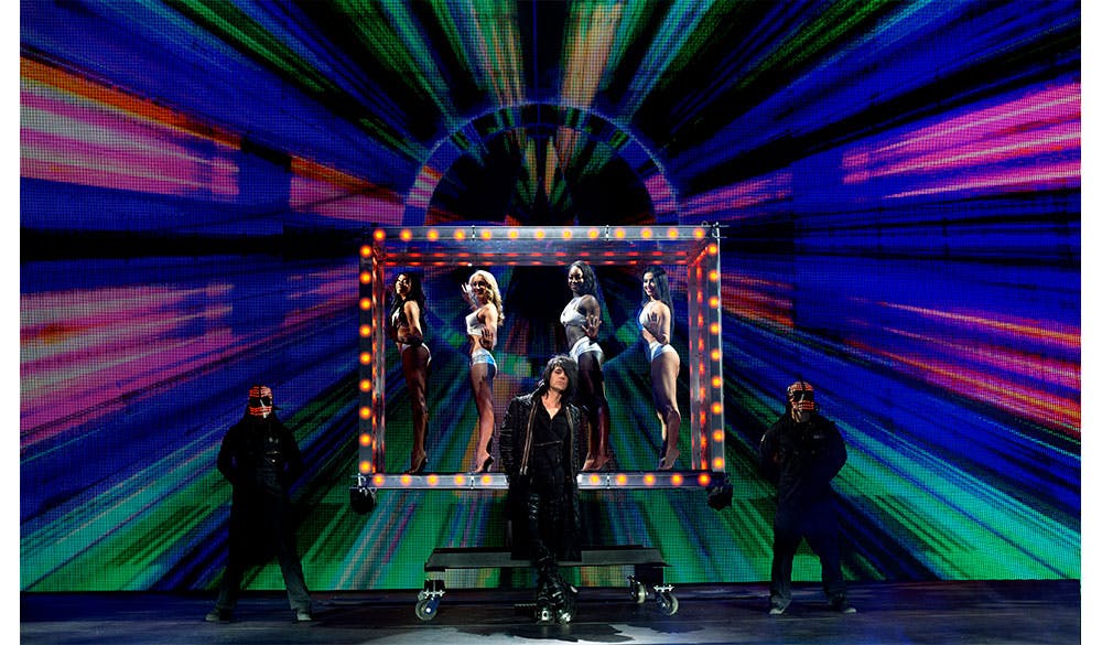 Criss Angel MINDFREAK stage performance — illuminated box frame with showgirls inside, multicolor LED wall backdrop and hooded figures at the Criss Angel Theater, Planet Hollywood