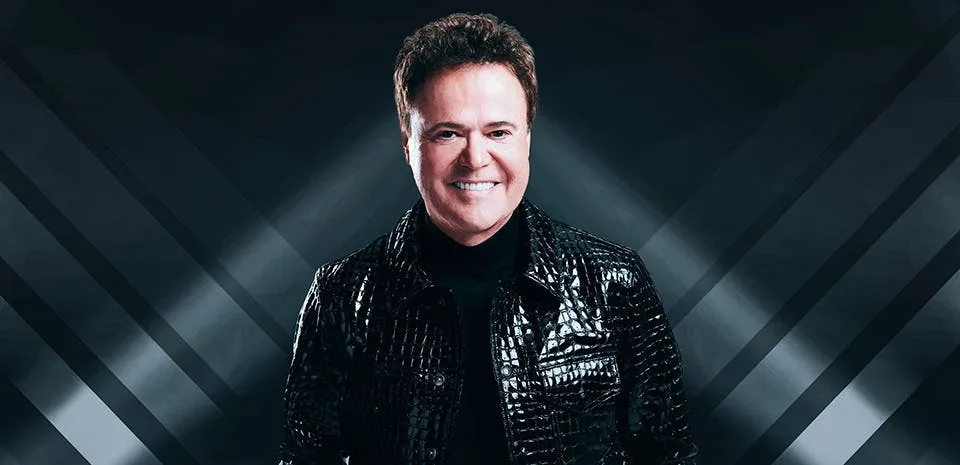 Donny Osmond in a black crocodile-print jacket against a dark spotlight backdrop