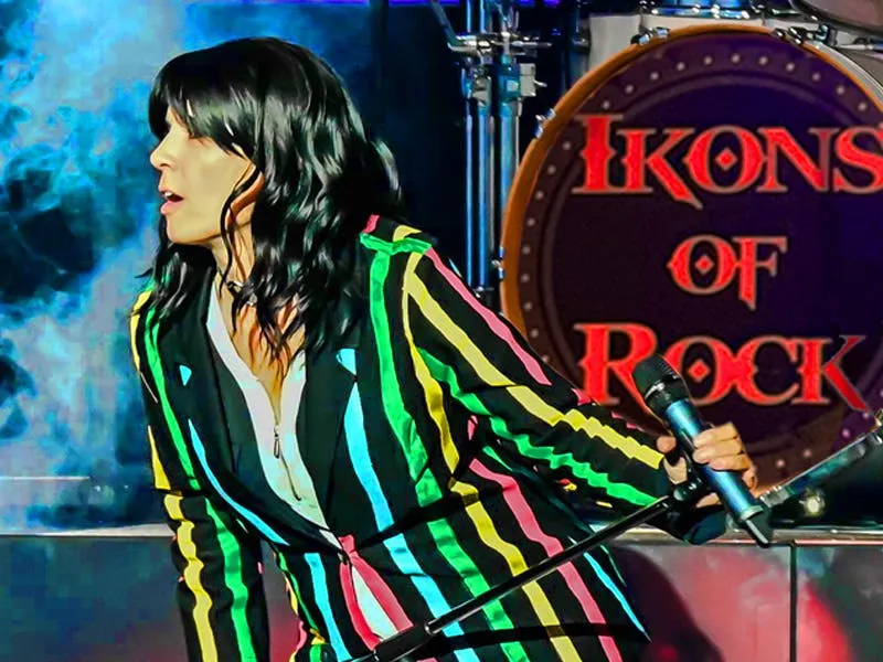 Ikons of Rock performer in a colorful striped suit singing in front of the Ikons of Rock drum riser