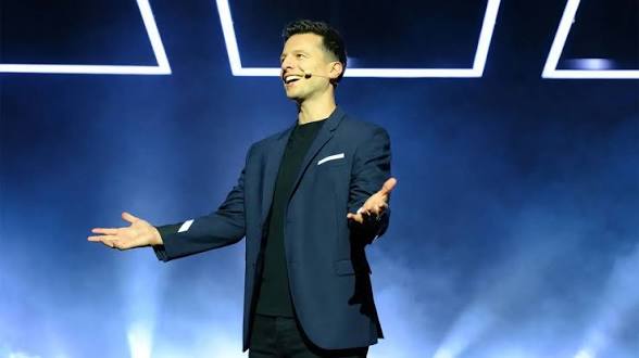 Mat Franco on stage at the Mat Franco Theater with arms outstretched, bathed in blue and purple stage lighting against a geometric LED backdrop at The LINQ Hotel Las Vegas