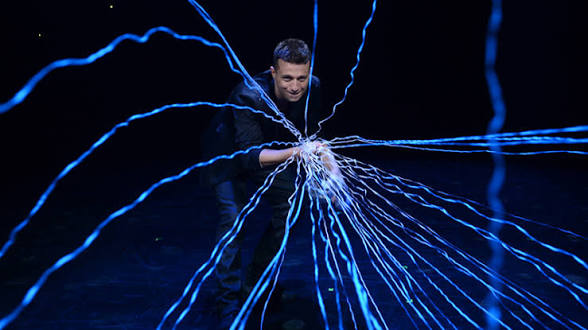 Mat Franco performing at the Mat Franco Theater with dramatic blue electric light and fiber optic effects exploding from his hands against a dark stage at The LINQ Hotel Las Vegas
