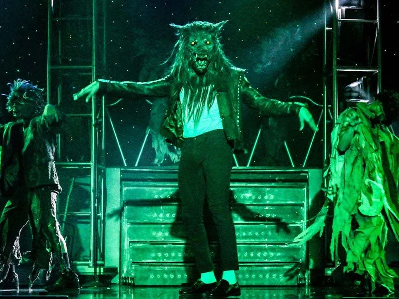 MJ Live Thriller number — performer in a werewolf mask with zombie dancers under green stage lighting