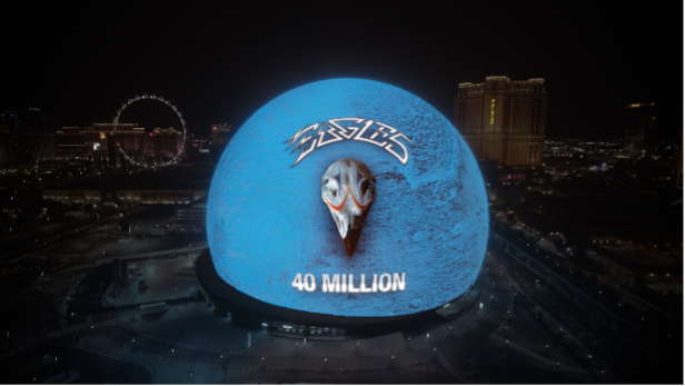 Sphere Las Vegas lit up in deep blue at night displaying the Eagles logo and '40 Million' to celebrate the band's Quadruple Diamond album certification milestone, with the Las Vegas Strip visible in the background