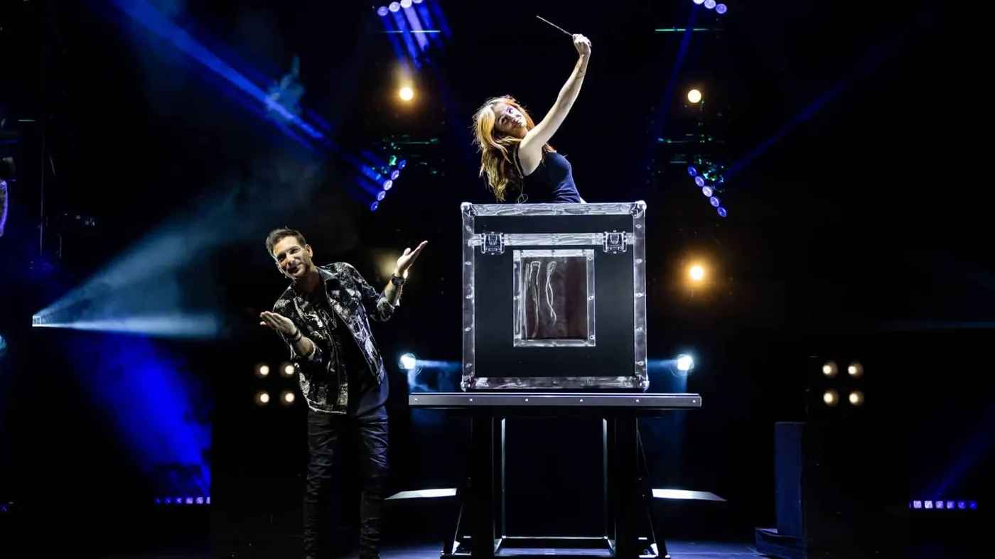 Now You See Me LIVE illusionists performing a trunk escape illusion on stage under blue lighting