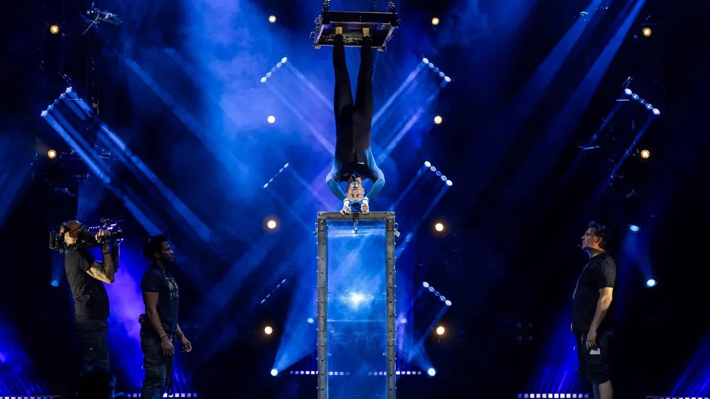 Now You See Me LIVE performer in a suspended upside-down escape stunt over a glass water tank