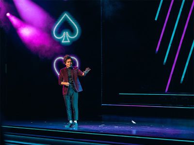 Shin Lim standing on the Palazzo Theatre stage during LIMITLESS Las Vegas, framed by a neon ace of spades and colorful stage lighting at The Venetian Resort
