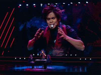 Shin Lim performing close-up card magic at a table on the Palazzo Theatre stage during LIMITLESS, his face projected on a large screen behind him at The Venetian Resort Las Vegas
