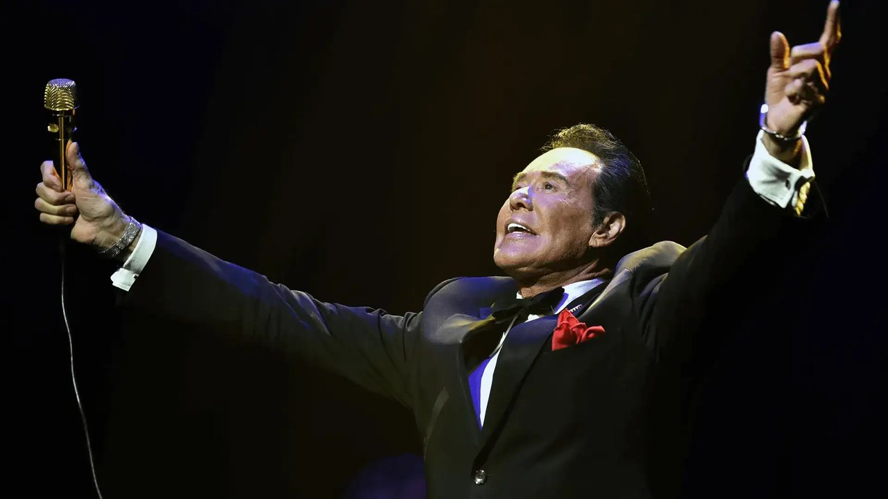 Wayne Newton performing on stage with a microphone, arms outstretched, at Bugsy's Cabaret Flamingo Las Vegas